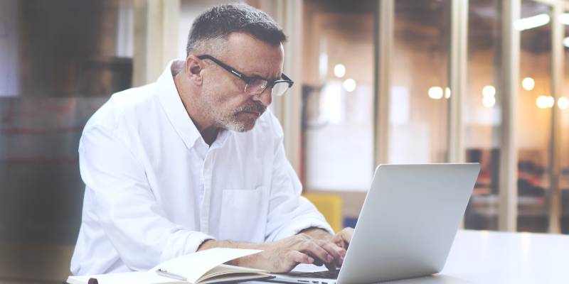 Aged man in white shirt working on his laptop