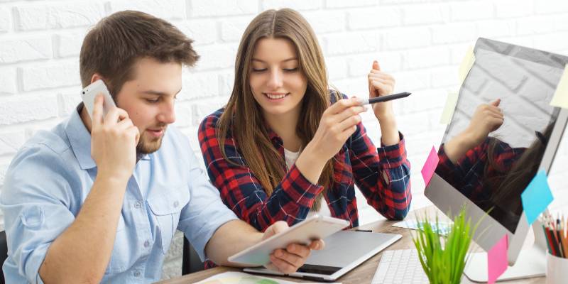 Man is talking on his mobile and woman in check shirt holding a pen and smiling