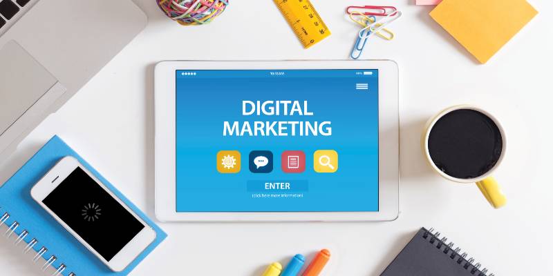 Digital marketing is written in a tablet on a table with a cup and mobile