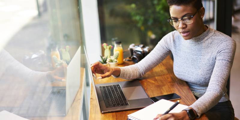 Woman is working in her laptop and writing something in a notebook